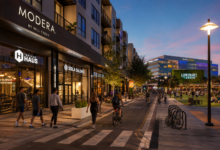 Street-level evening view of Modera Creative Village, active retail storefronts, pedestrians and cyclists beside Luminary Green in Downtown Orlando.