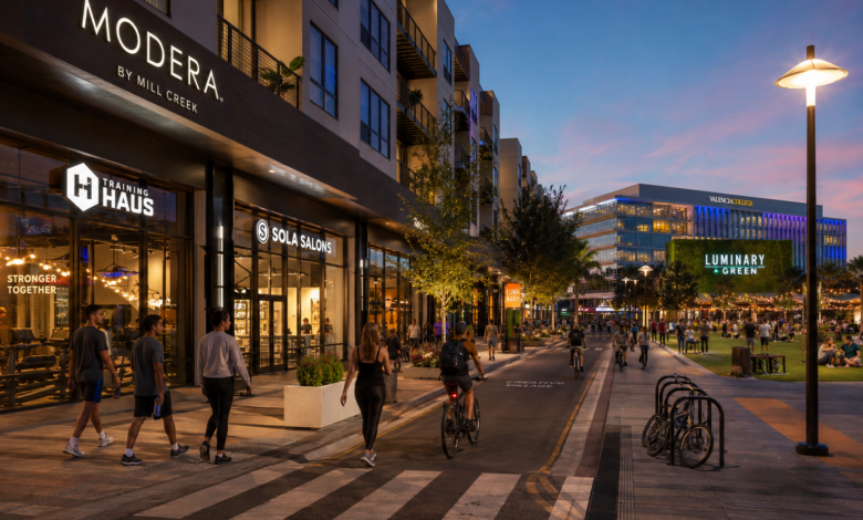Street-level evening view of Modera Creative Village, active retail storefronts, pedestrians and cyclists beside Luminary Green in Downtown Orlando.